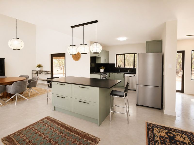 Spacious open-plan kitchen and dining area featuring a central island, modern sage green cabinetry, and polished concrete flooring with abundant natural light.