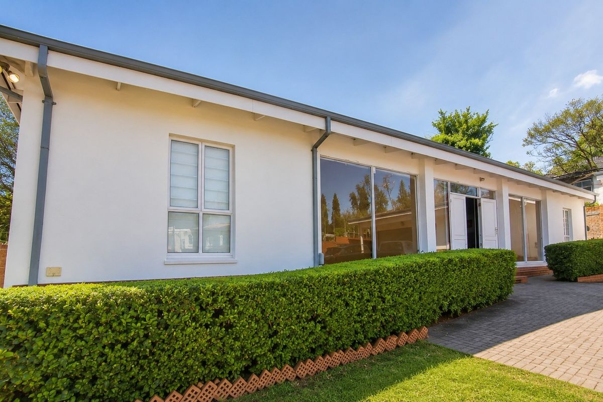 A well-maintained rear exterior view featuring a paved driveway, manicured hedge, and large sliding glass doors providing access to the home.