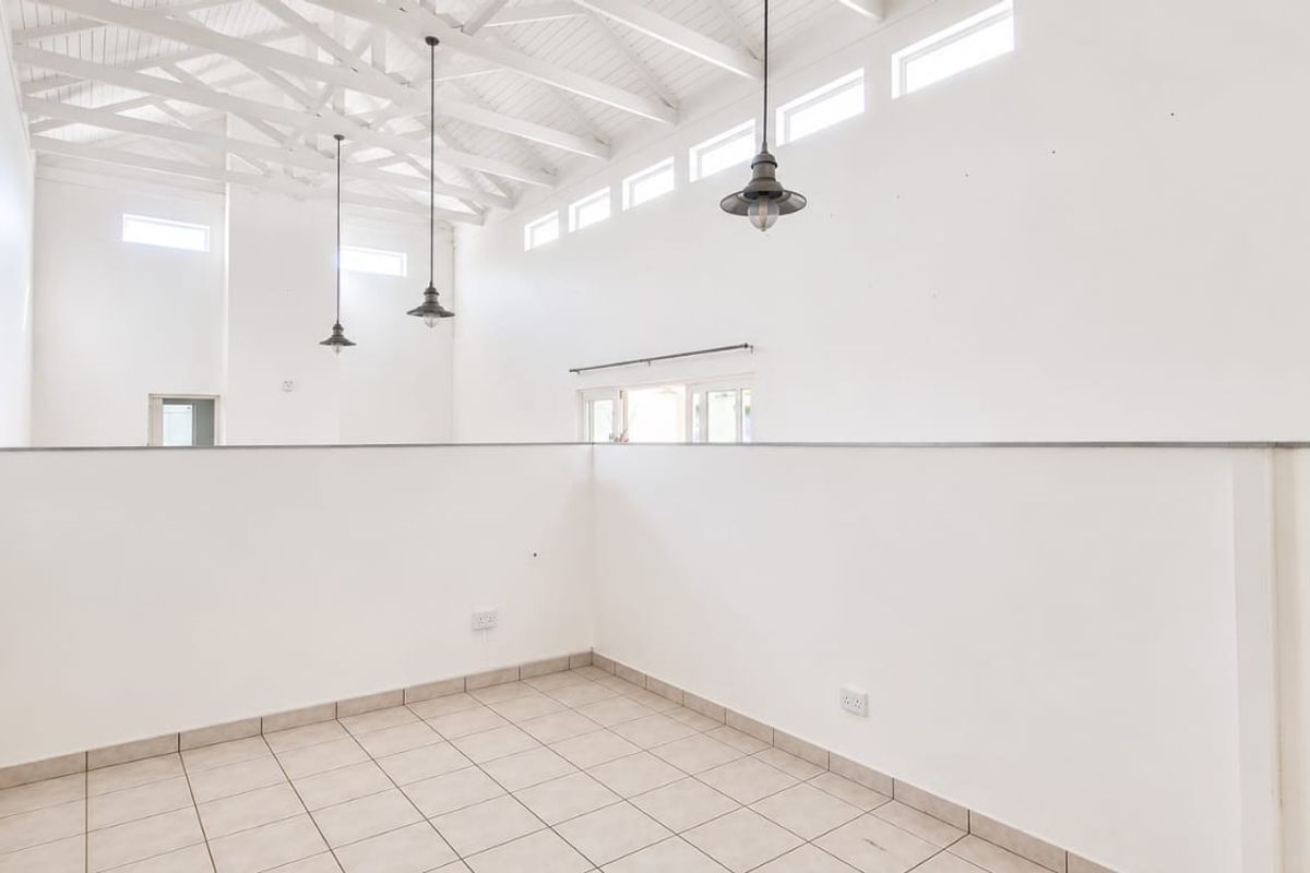 Spacious living area featuring high vaulted ceilings with exposed timber trusses, ceramic tiled flooring, and abundant natural light from clerestory windows.