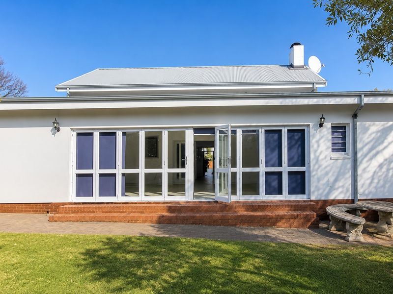 Rear elevation of the house featuring a paved patio, white-framed glass folding doors, and a well-maintained garden area.