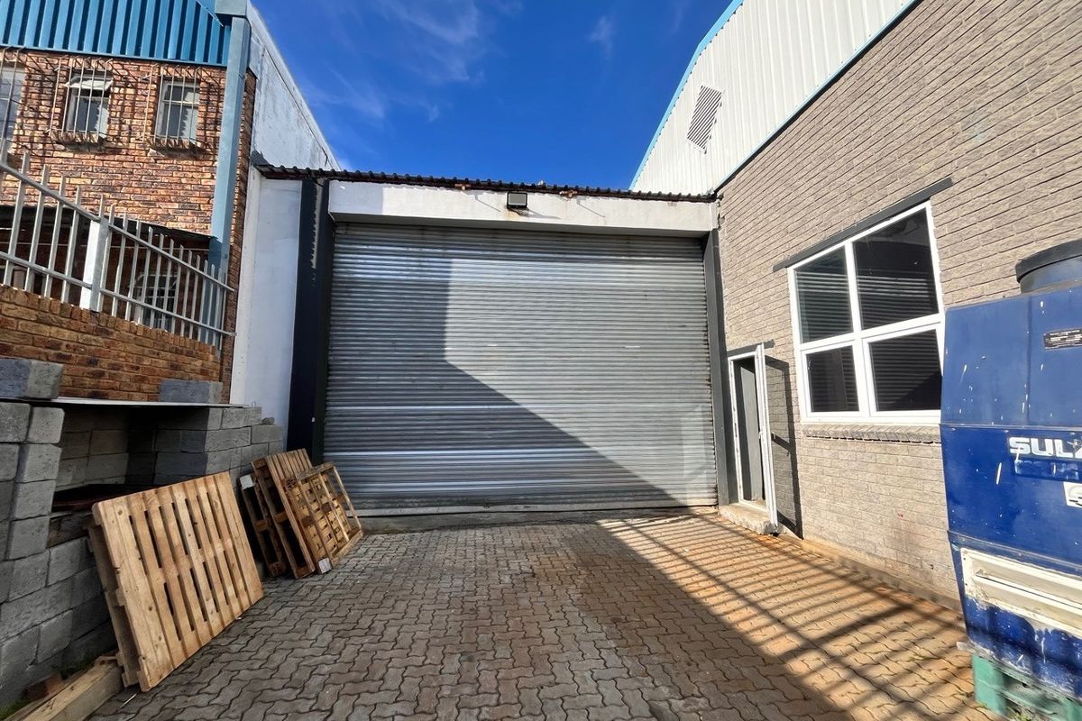 Rear industrial yard area featuring a large roller shutter door, paved access, and brick exterior walls with security window bars.