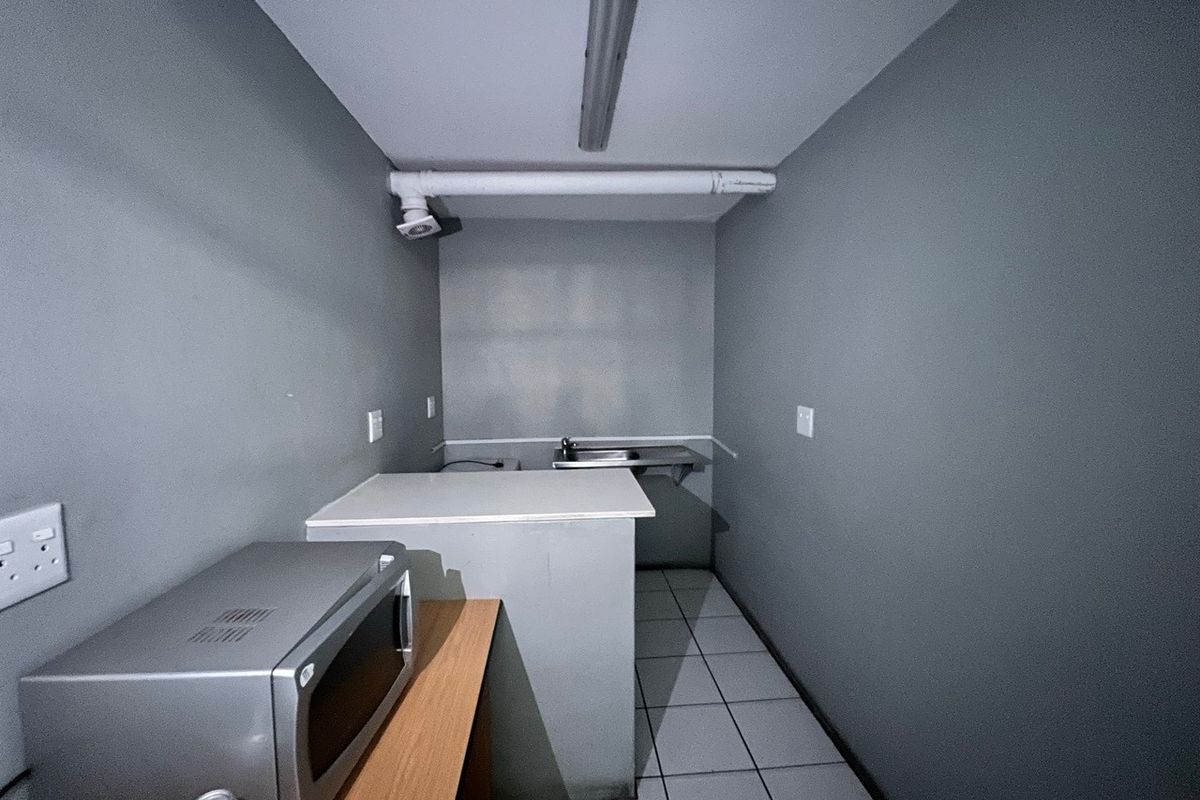 A compact industrial kitchenette featuring tiled flooring, a stainless steel sink, and basic utility lighting.