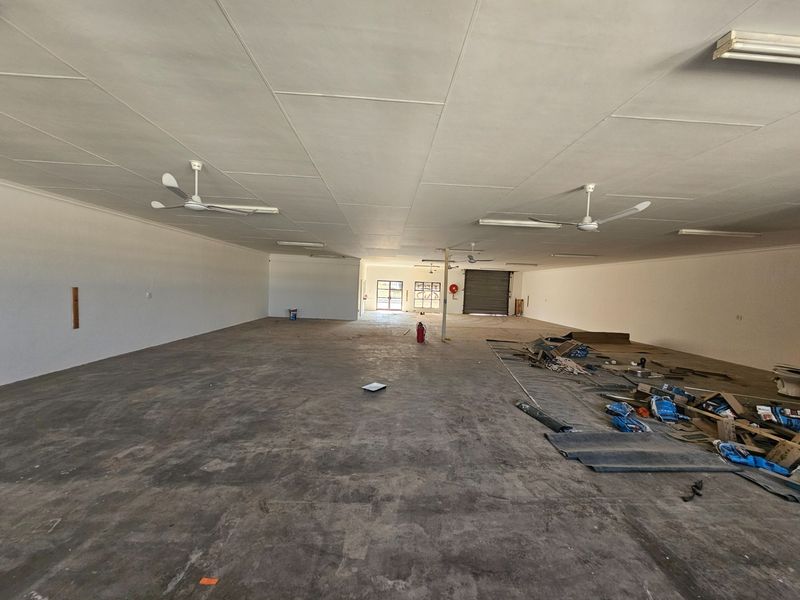 A large, open-plan commercial space featuring concrete flooring, ceiling fans, and a rear roller shutter door, suitable for various business applications.