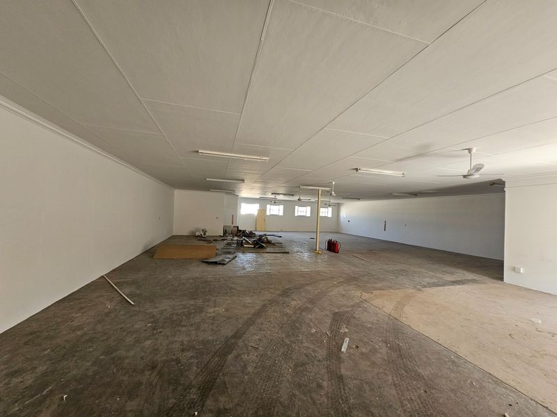 A large, open-plan commercial space featuring concrete flooring, ceiling fans, and fluorescent lighting, suitable for various business or retail configurations.
