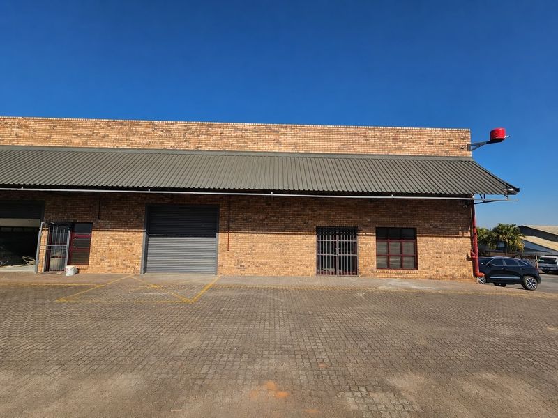 Commercial warehouse exterior featuring a face brick facade, corrugated metal awning, roller shutter door, and paved driveway access.