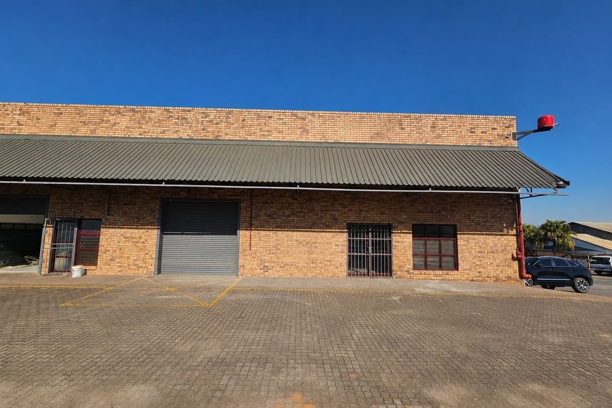 Commercial warehouse exterior featuring a face brick facade, corrugated metal awning, roller shutter door, and paved driveway access.