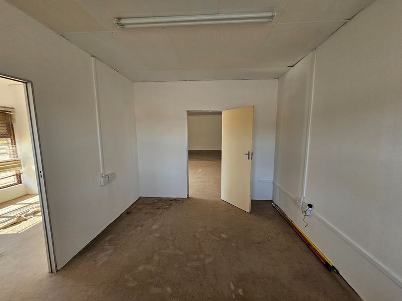 An empty, utilitarian office space featuring suspended ceiling tiles, surface-mounted electrical conduits, and worn flooring, ready for renovation or commercial fit-out.