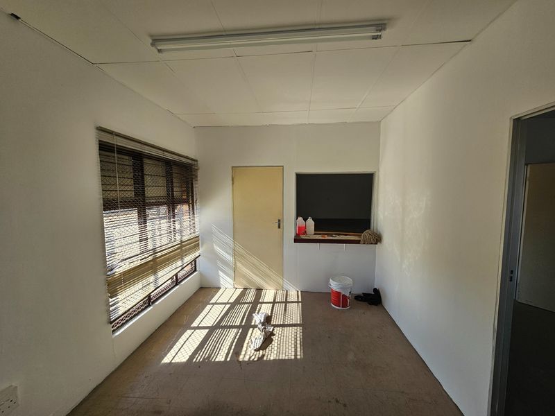 An empty commercial office space featuring a service hatch, venetian blinds, and a suspended ceiling, suitable for various business or administrative uses.