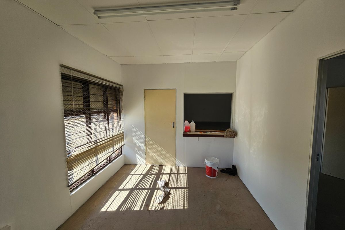 An empty commercial office space featuring a service hatch, venetian blinds, and a suspended ceiling, suitable for various business or administrative uses.