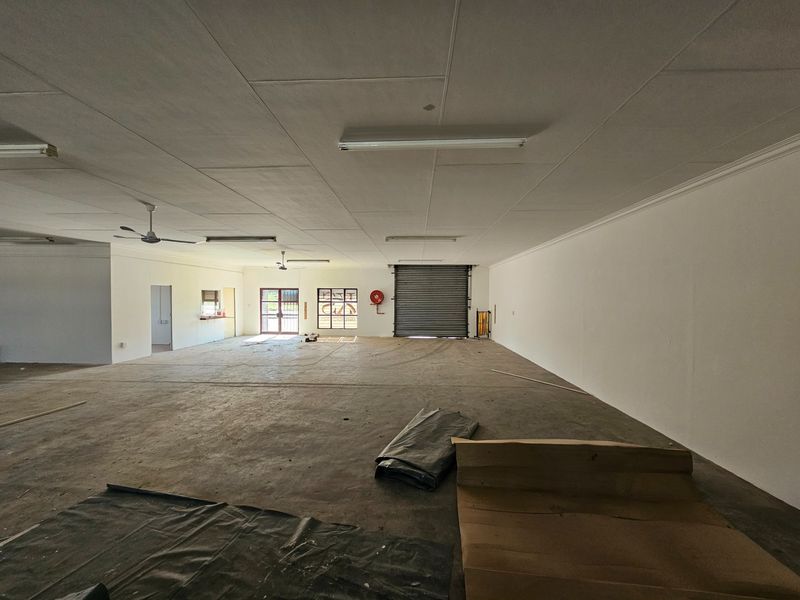 Spacious open-plan commercial unit featuring concrete flooring, roller shutter access, and functional ceiling lighting, suitable for various retail or industrial business applications.