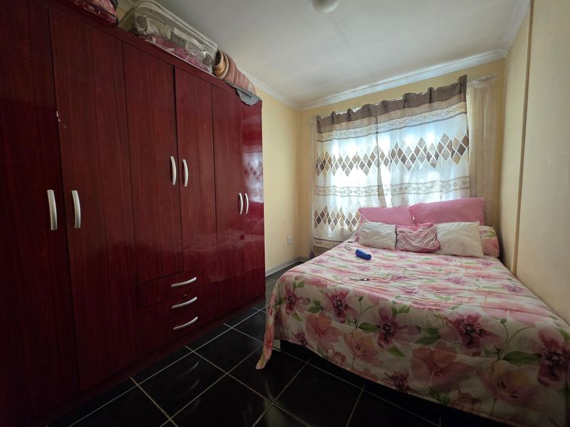 A bedroom featuring dark tiled flooring, a large built-in wardrobe, and a window with curtains.
