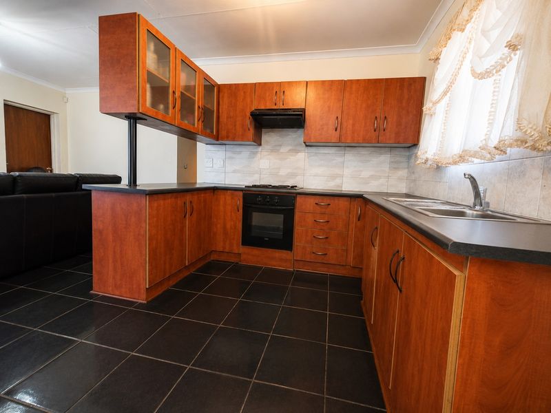 A functional kitchen featuring wood-look laminate cabinetry, dark countertops, built-in oven with gas hob, and tiled flooring.