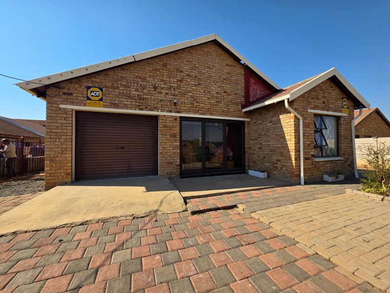 Front elevation of a face brick house featuring a single garage, paved driveway, and aluminium sliding door entrance.