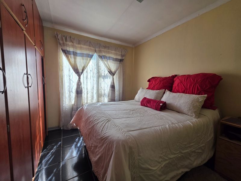 A bedroom featuring built-in wooden cupboards and dark tiled flooring, providing a functional space with natural light.