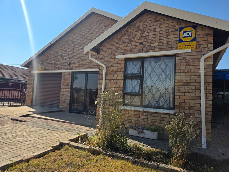 Front elevation of a face brick house featuring a roller shutter garage door, aluminium sliding entrance, and paved driveway area.