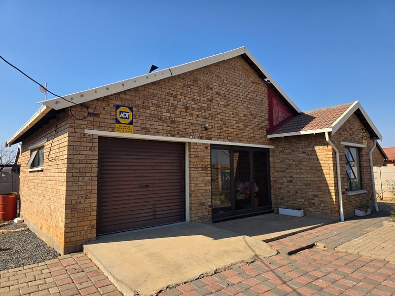 Front elevation of a face brick house featuring a roller garage door, aluminium windows, and a paved driveway area.