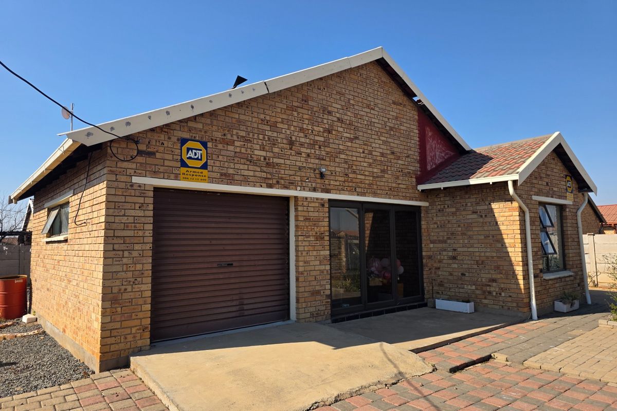 Front elevation of a face brick house featuring a roller garage door, aluminium windows, and a paved driveway area.