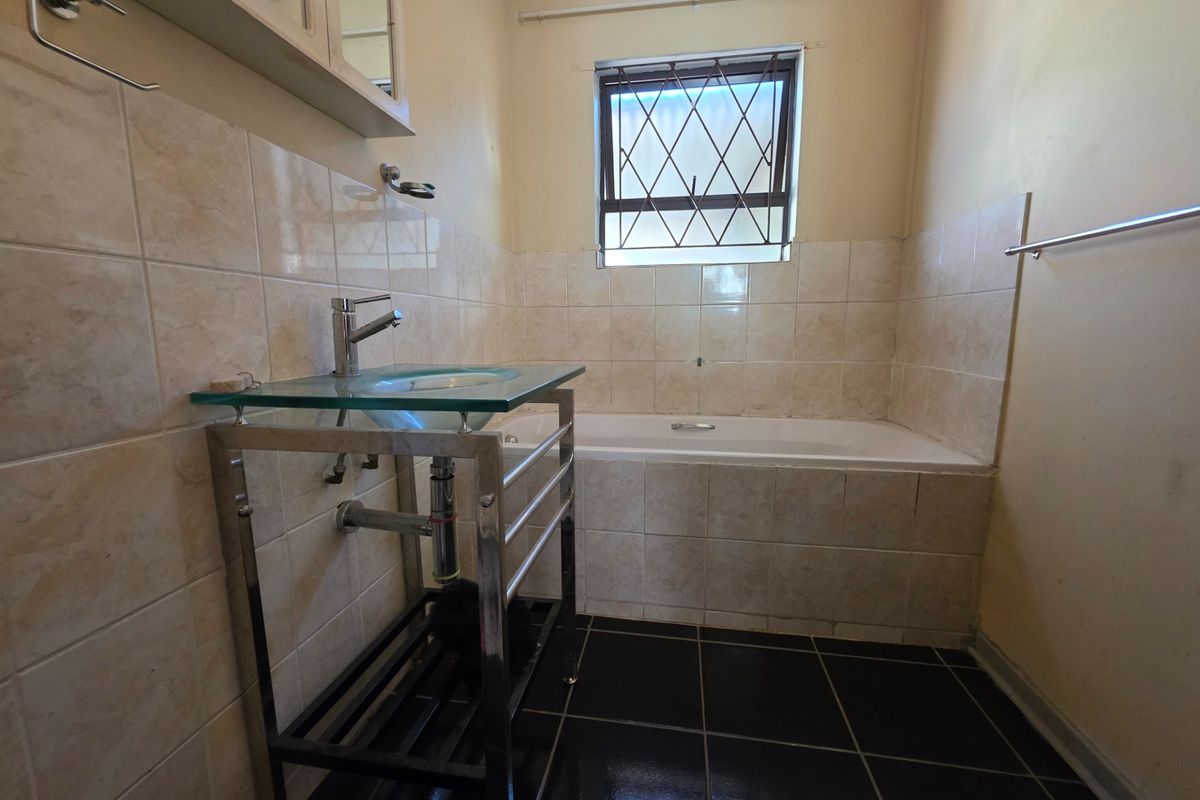 A dated bathroom featuring a built-in bathtub, tiled walls, and a glass vanity basin with metal security bars on the window.