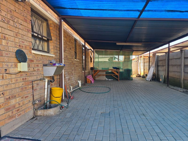 Covered outdoor patio area featuring brick exterior walls, paved flooring, and a functional utility sink, providing a versatile space for outdoor activities.