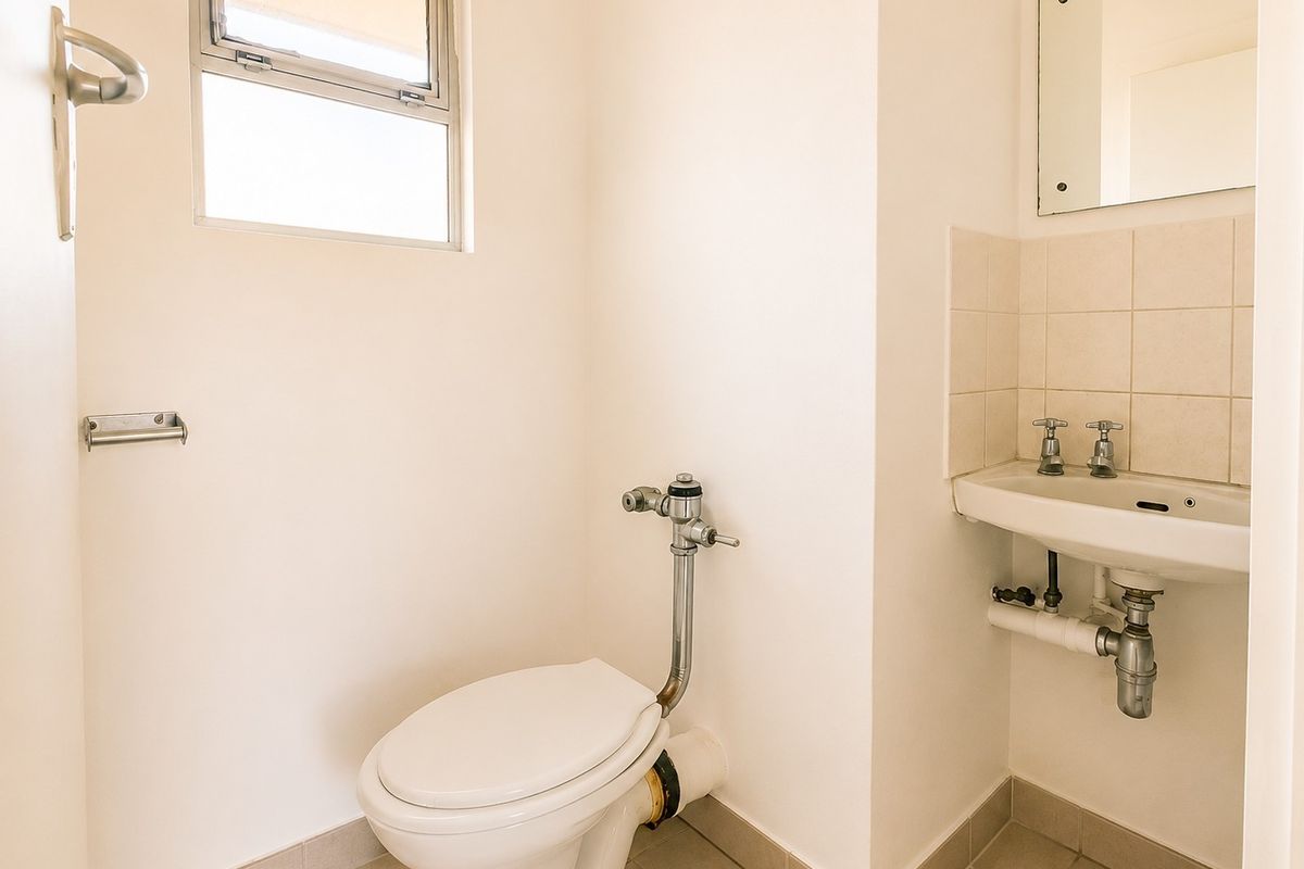 A functional bathroom featuring a wall-mounted basin with tiled splashback, a flush valve toilet, and tiled flooring.
