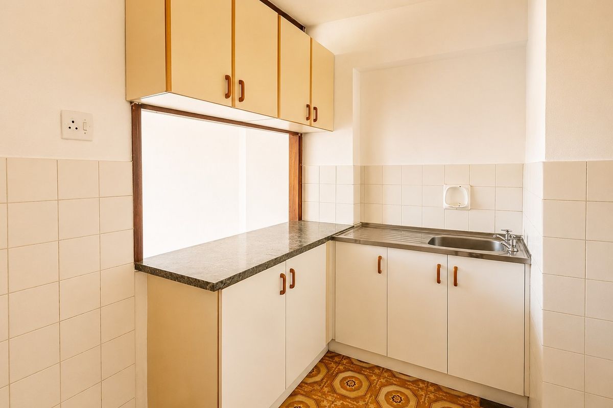 A compact, empty kitchen featuring dated patterned floor tiles, white cabinetry, laminate countertops, and a stainless steel sink with tiled splashback.