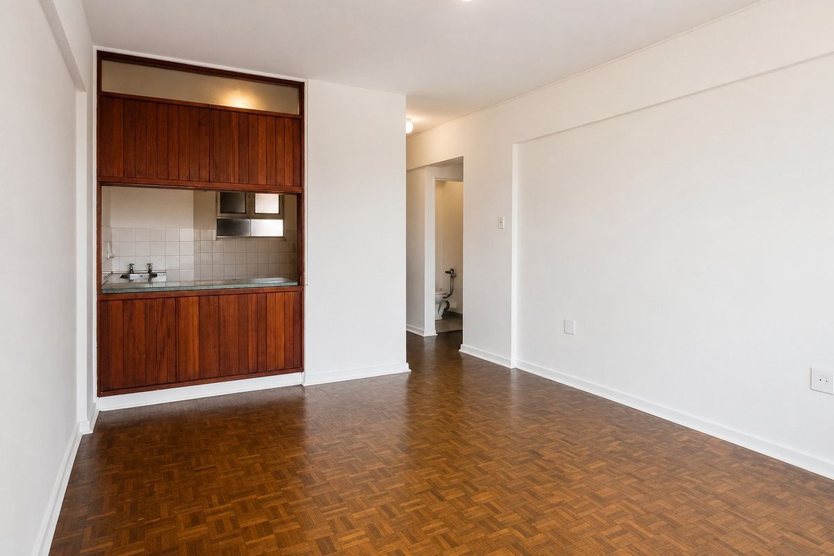 An empty living area featuring original parquet flooring and a built-in wooden cabinetry unit with a convenient kitchen pass-through window.