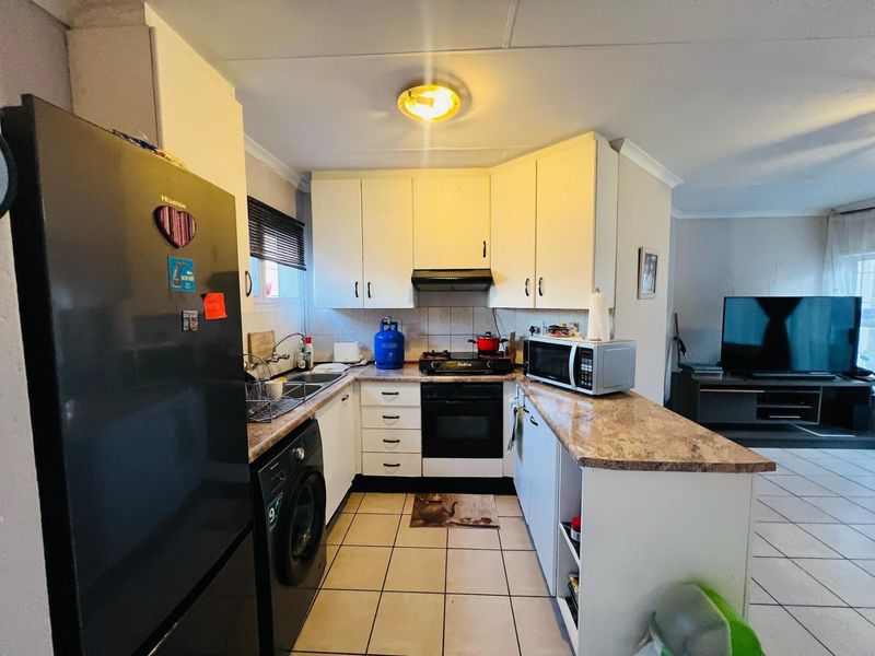 Open-plan kitchen featuring built-in cabinetry, laminate countertops, integrated oven and hob, and tiled flooring, flowing into the adjacent living area.