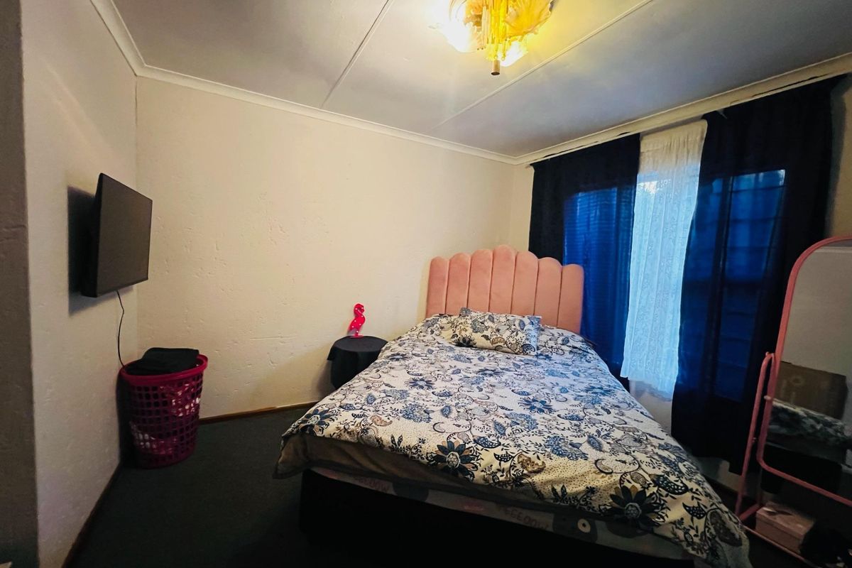 A bedroom featuring a ceiling light fixture and window curtain rails, requiring cosmetic updates to the wall finishes and flooring.