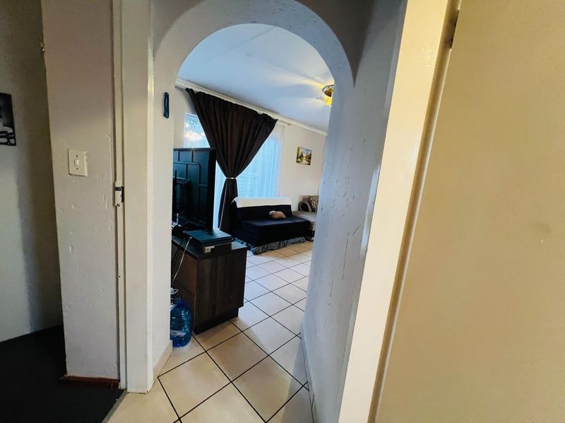 A view through an arched doorway into a living area featuring ceramic floor tiles and dated wall finishes.