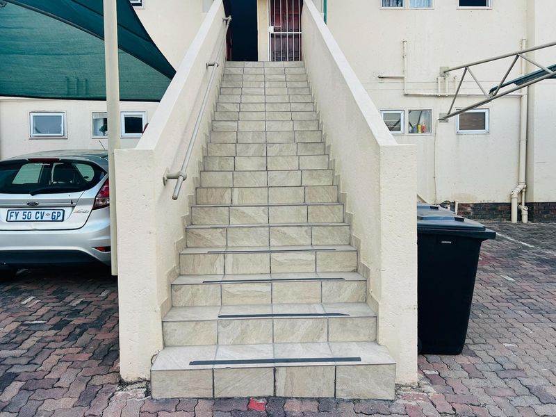 Exterior view of an apartment building entrance featuring a tiled staircase with a metal handrail and security gate access.