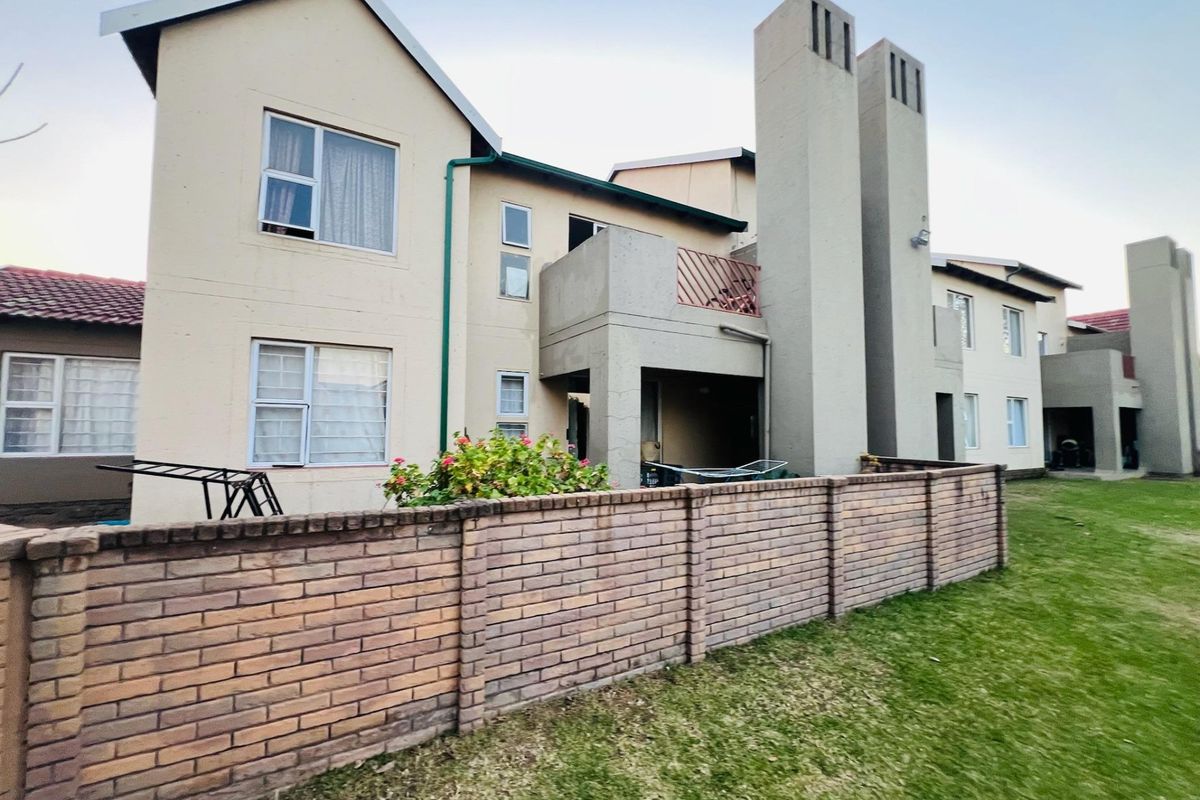 Rear view of a multi-story apartment complex featuring brick boundary walls, private balconies, and prominent chimney stacks set against a communal lawn area.