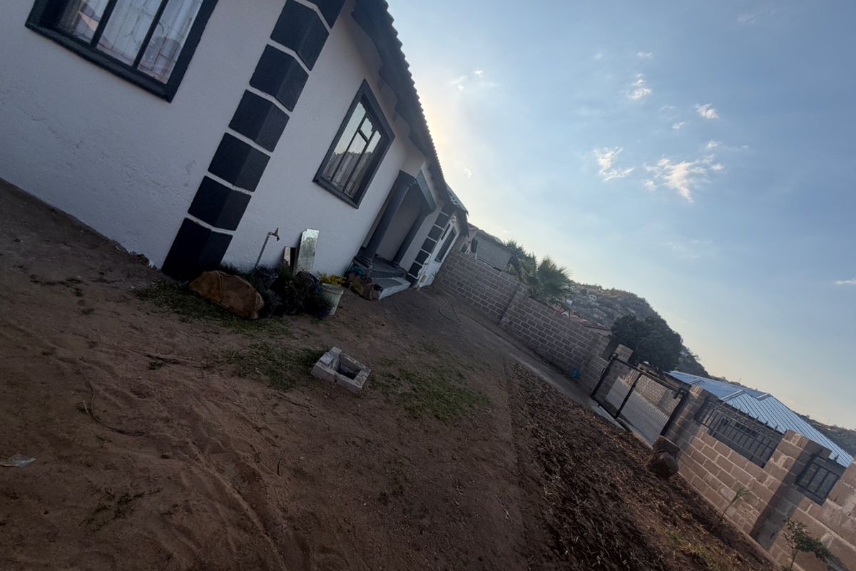Rear exterior view of the property featuring a concrete block boundary wall, metal gate, and an unlandscaped yard area.
