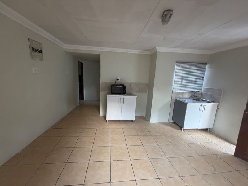 A basic, functional kitchen area featuring tiled flooring, simple base cabinetry, a sink, and tiled splashbacks, offering potential for modernization.