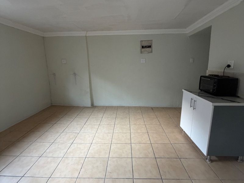 An empty kitchen area featuring tiled flooring, basic base cabinetry, and visible ceiling and wall wear, offering a blank canvas for renovation.