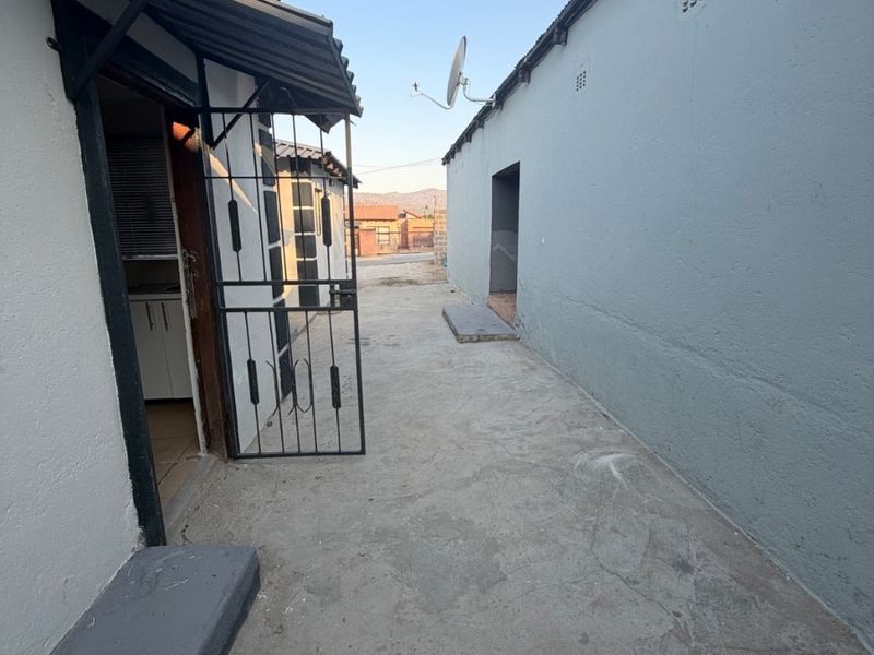 A narrow exterior side passage between two structures featuring concrete paving, a security gate, and a satellite dish mounted on the wall.