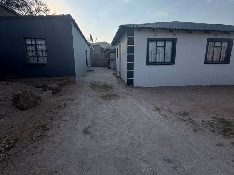Rear view of the property showing two separate structures with a central concrete pathway and unpaved dirt yard area.