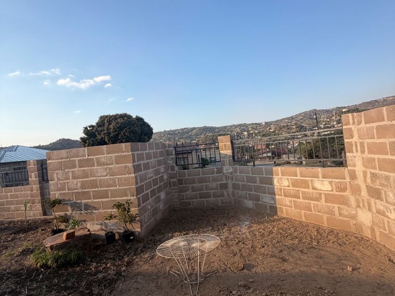 An outdoor garden area featuring a brick boundary wall and metal fencing, currently awaiting landscaping and ground finishing.