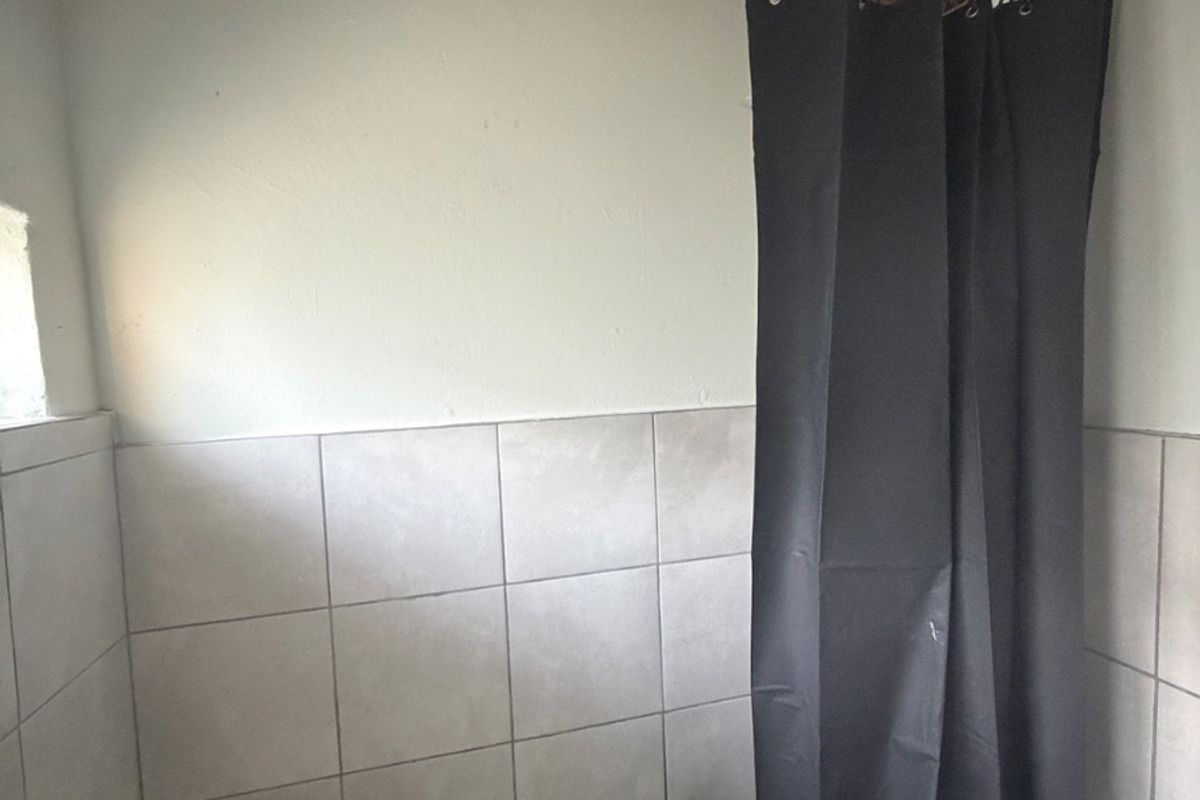 A shower area featuring tiled walls and flooring, with exposed timber ceiling beams and visible ceiling damage requiring repair.