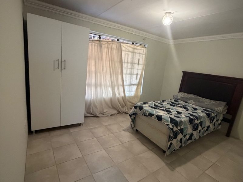 A bedroom featuring tiled flooring, cornicing, and a built-in wardrobe, providing a functional space with security bars on the window.