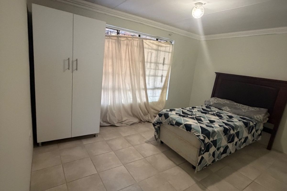 A bedroom featuring tiled flooring, cornicing, and a built-in wardrobe, providing a functional space with security bars on the window.