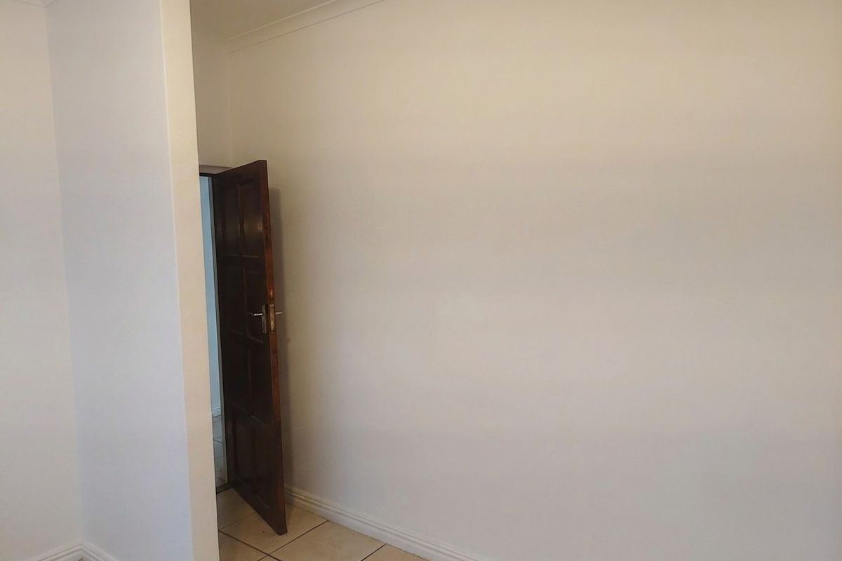 A clean, empty bedroom featuring neutral tiled flooring, coved ceilings, and a classic timber door, providing a blank canvas for personalization.