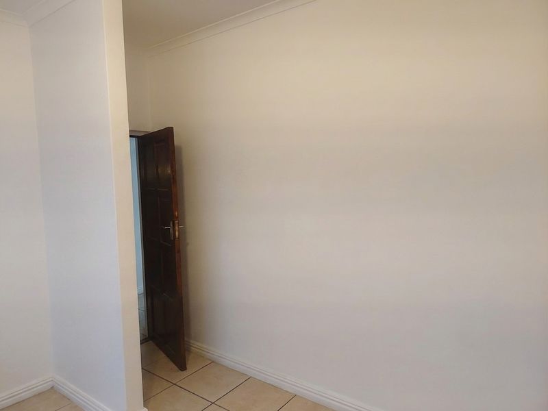 A clean, empty bedroom featuring neutral tiled flooring, coved ceilings, and a classic timber door, providing a blank canvas for personalization.