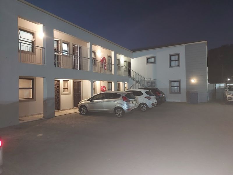 Exterior view of a multi-story apartment complex at night, featuring paved parking, external staircases, and balcony access to individual units.