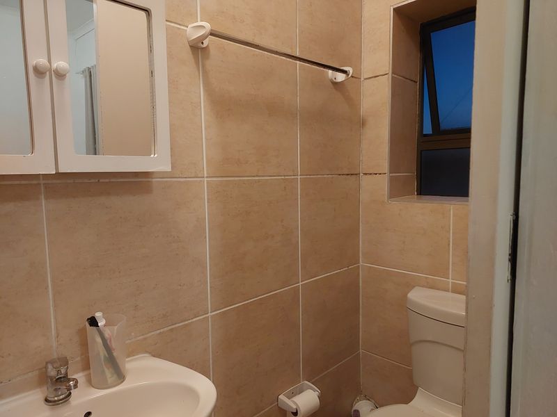 Compact bathroom featuring neutral wall tiles, a pedestal basin with chrome mixer, and a top-flush toilet, providing a functional and practical space.