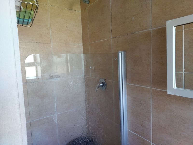 A functional bathroom shower area featuring beige ceramic wall tiles, a glass shower screen, and a built-in medicine cabinet.