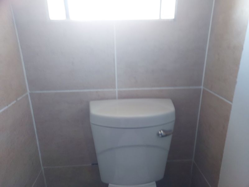 A compact bathroom space featuring a standard toilet and neutral ceramic wall tiling.