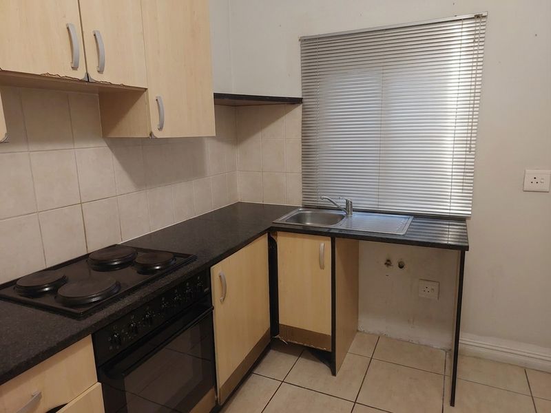 Compact kitchen featuring built-in cabinetry, electric hob and oven, stainless steel sink, and tiled finishes, requiring minor cosmetic updates.
