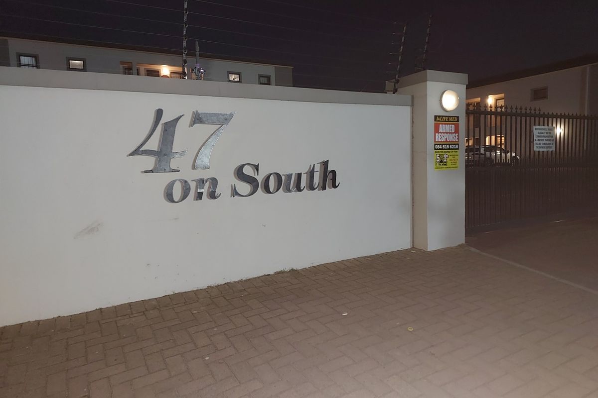 Night view of the entrance to 47 on South, featuring a secure boundary wall, electric fencing, and a gated access point.
