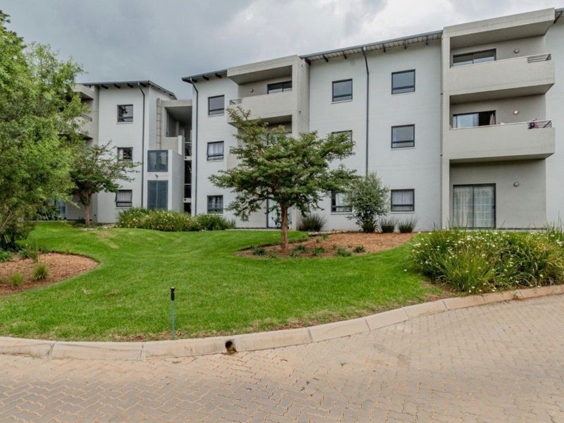 Exterior view of a modern apartment complex featuring multi-level balconies, paved driveway access, and well-maintained communal garden areas.