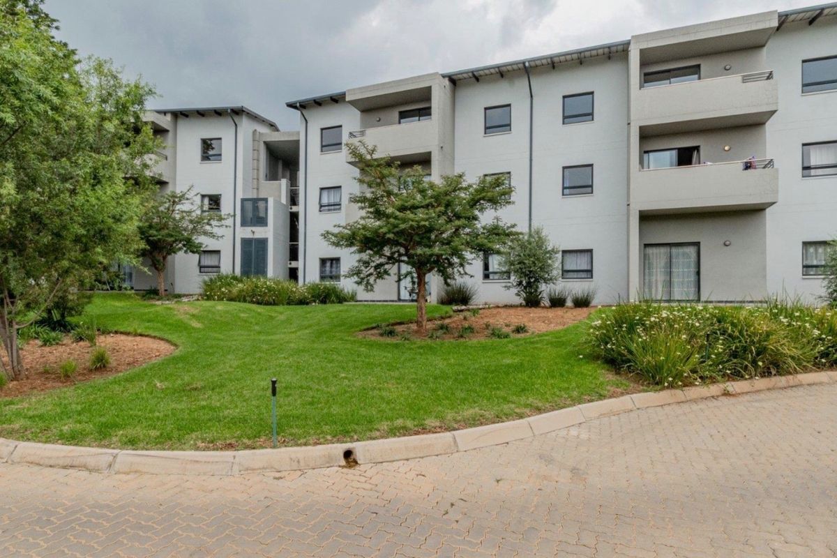 Exterior view of a modern apartment complex featuring multi-level balconies, paved driveway access, and well-maintained communal garden areas.